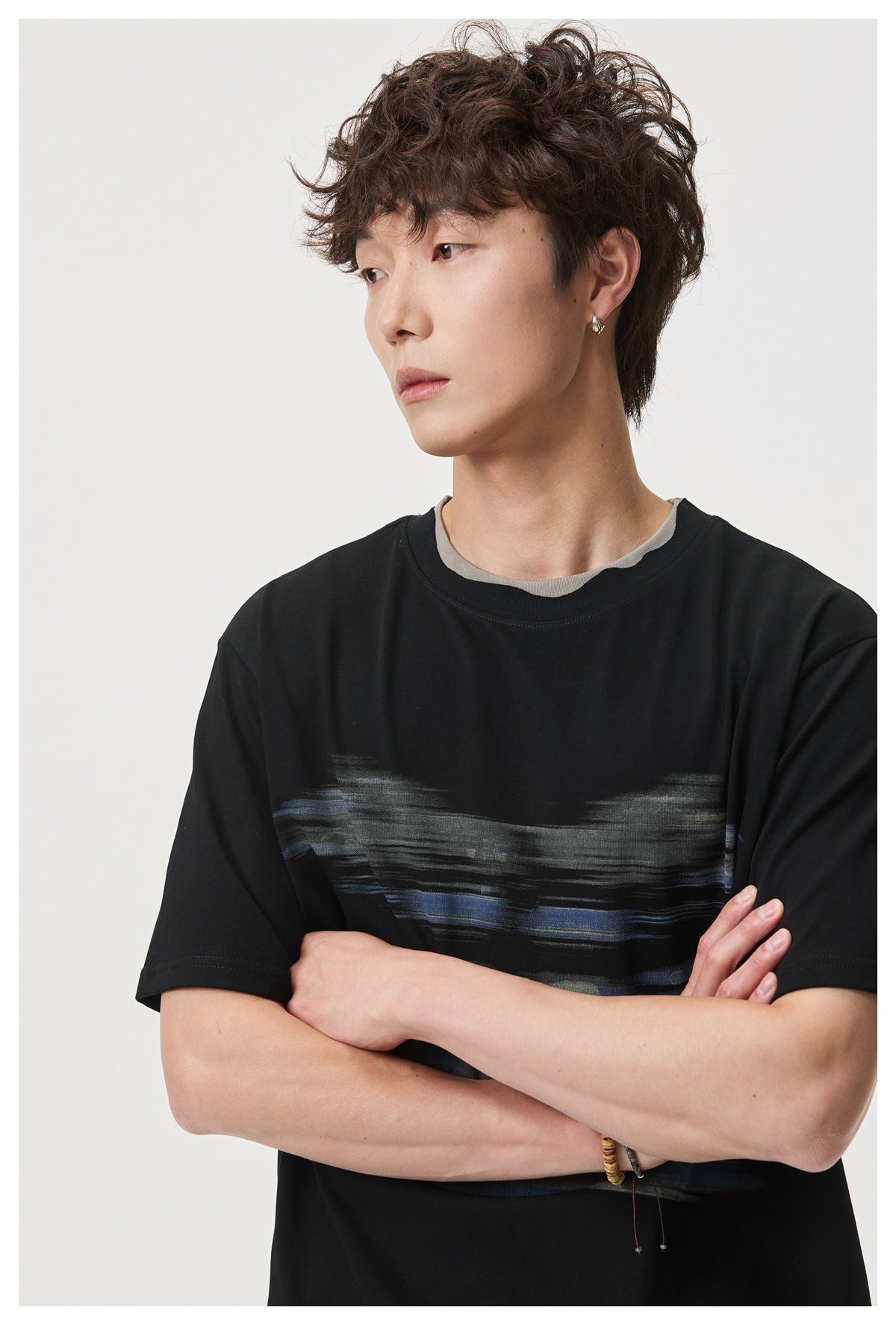 Close view of a model wearing a black short-sleeve T-shirt with gray and blue brushstroke artwork and a gray layered