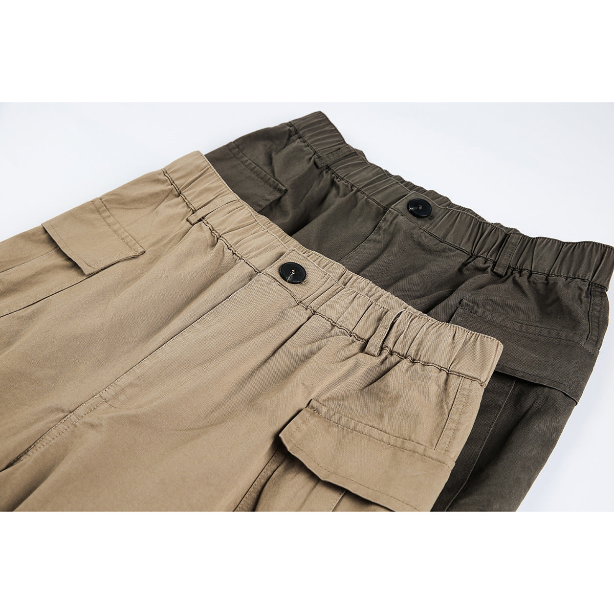 Close-up of tan and dark olive cargo pants showing elastic waistbands, black buttons and flap pockets.