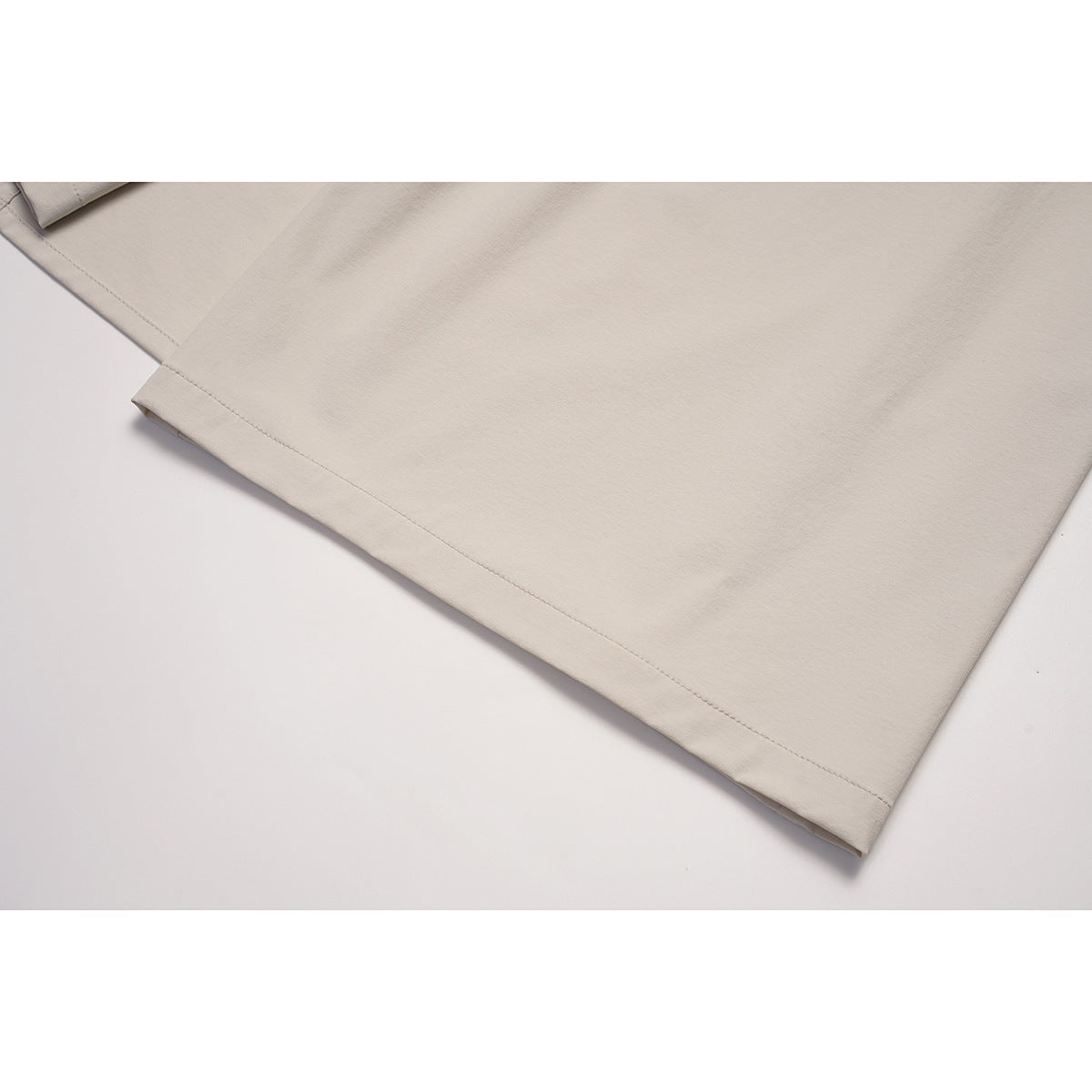 Close-up of the beige skirt's plain fabric and stitched hem.