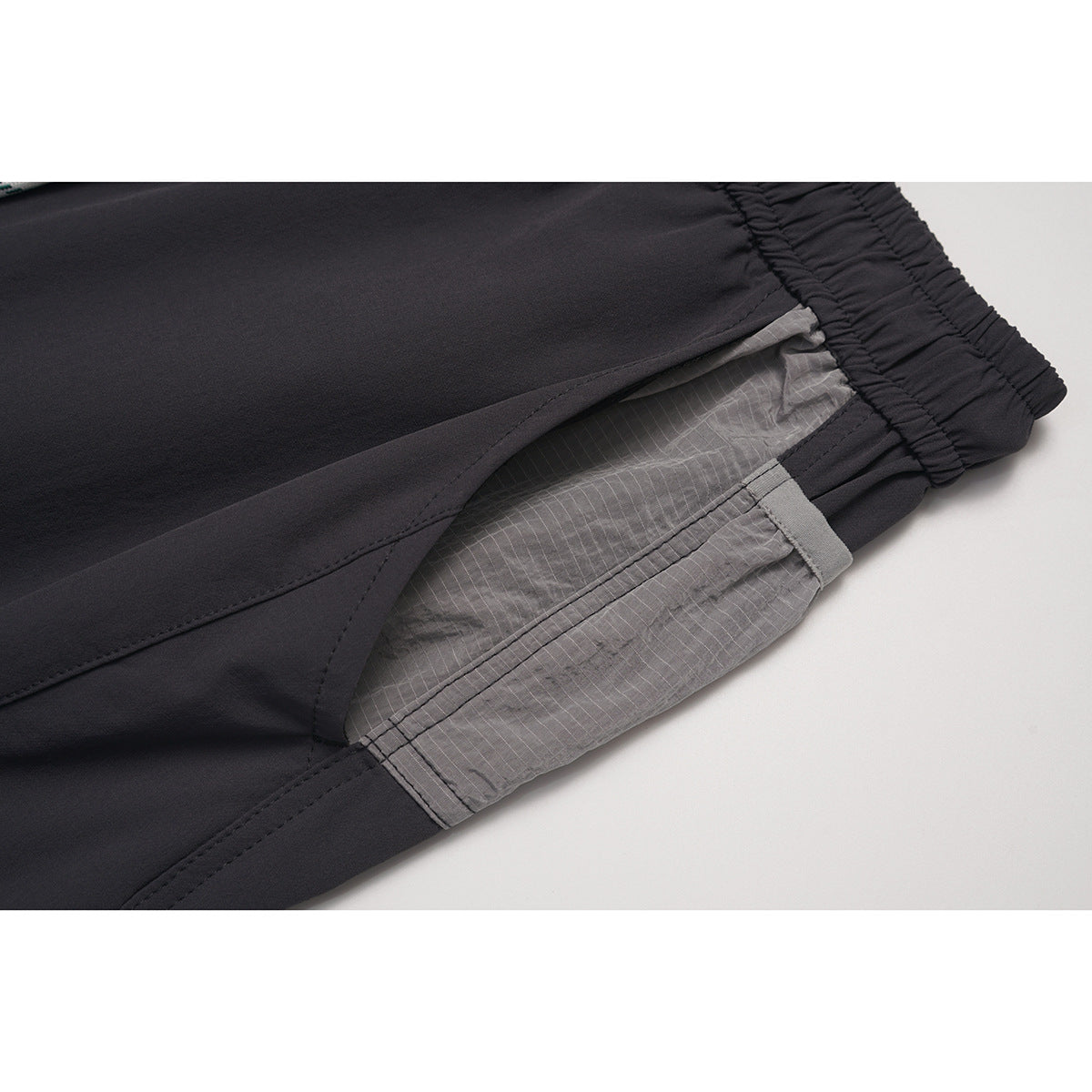 Close-up of charcoal pants showing a gray patterned side panel and stitched seams.