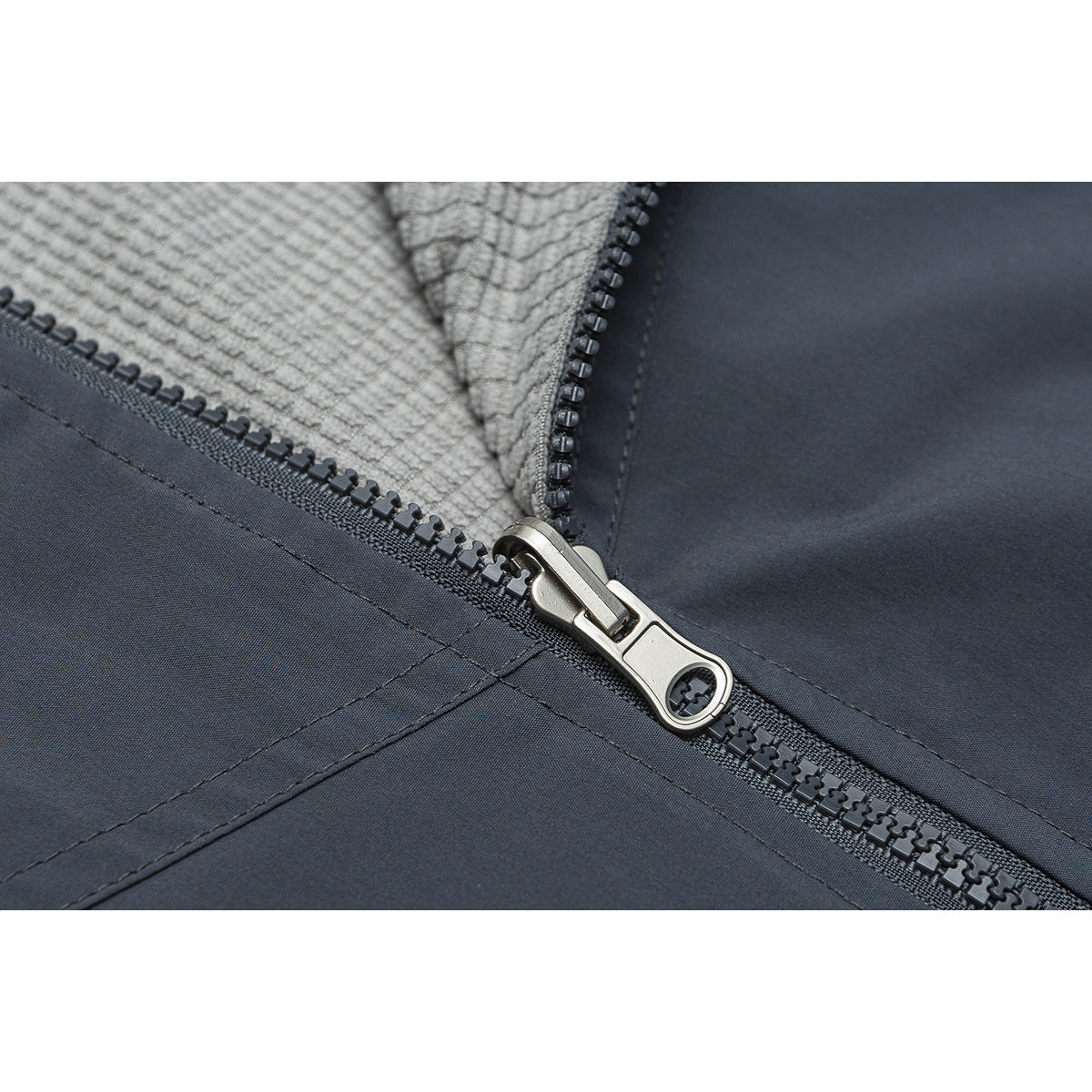 Close-up of a dark gray jacket zipper and metal pull, with textured light gray lining visible.