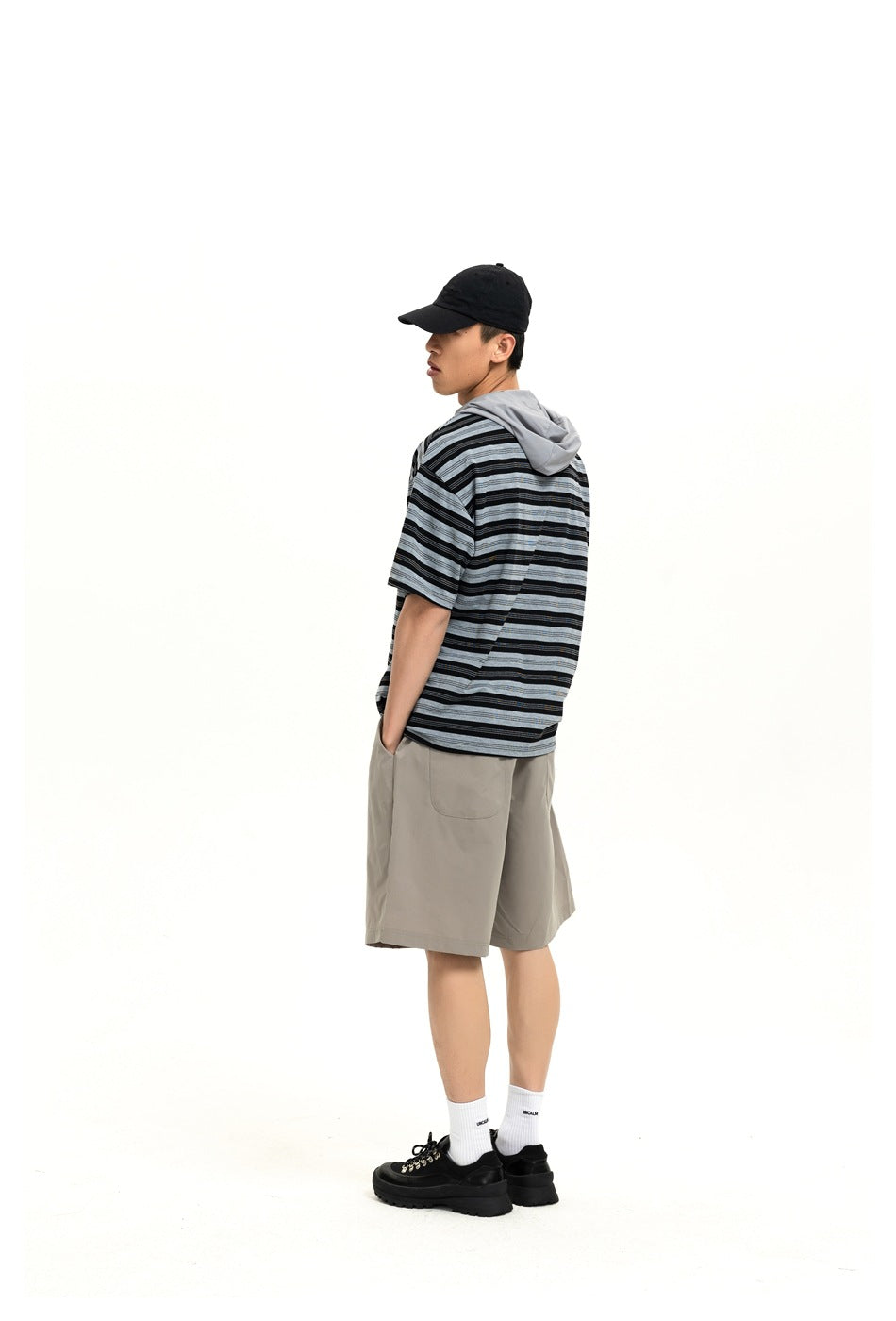 Back view of a model in gray wide-leg shorts with a patch back pocket, striped hooded tee and cap
