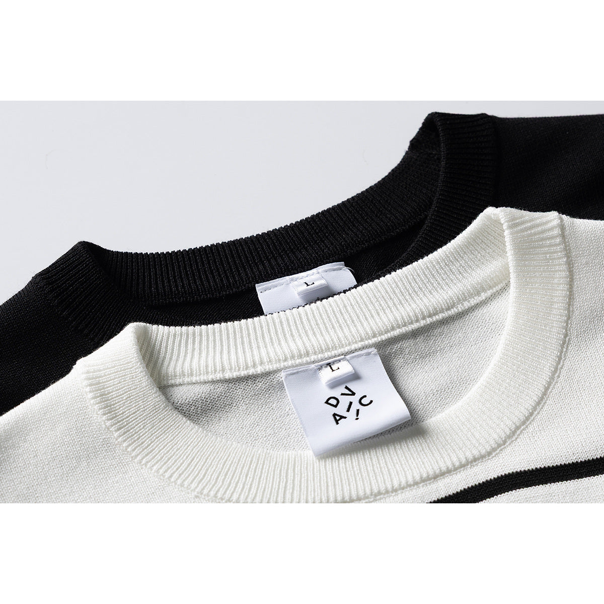 Close-up of black and ivory striped knit tops showing their ribbed crew necks and sewn-in labels.