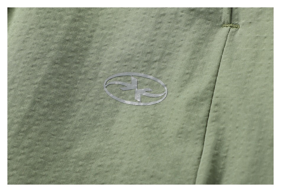 Close-up of a small silver oval logo on the sage green skirt fabric.