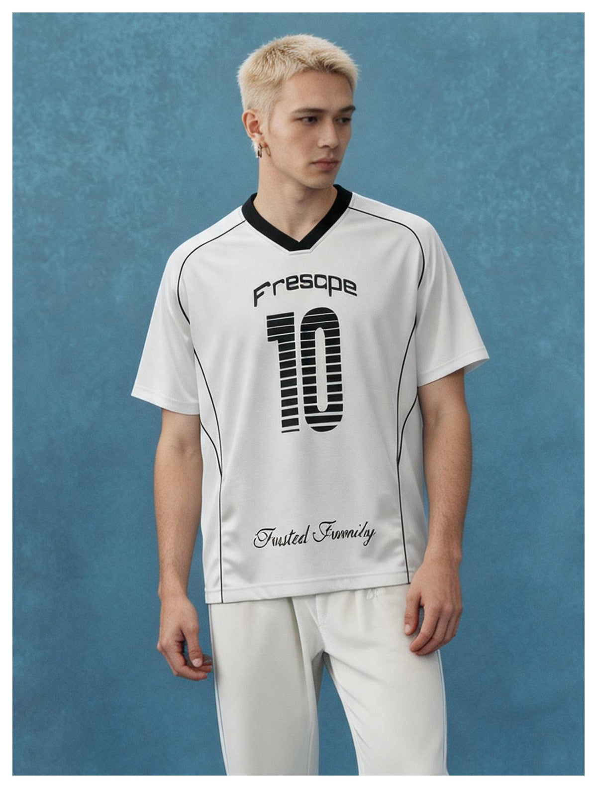 Man with short blond hair wearing a white V-neck jersey T-shirt with black trim and printed number 10 against a blue backdrop