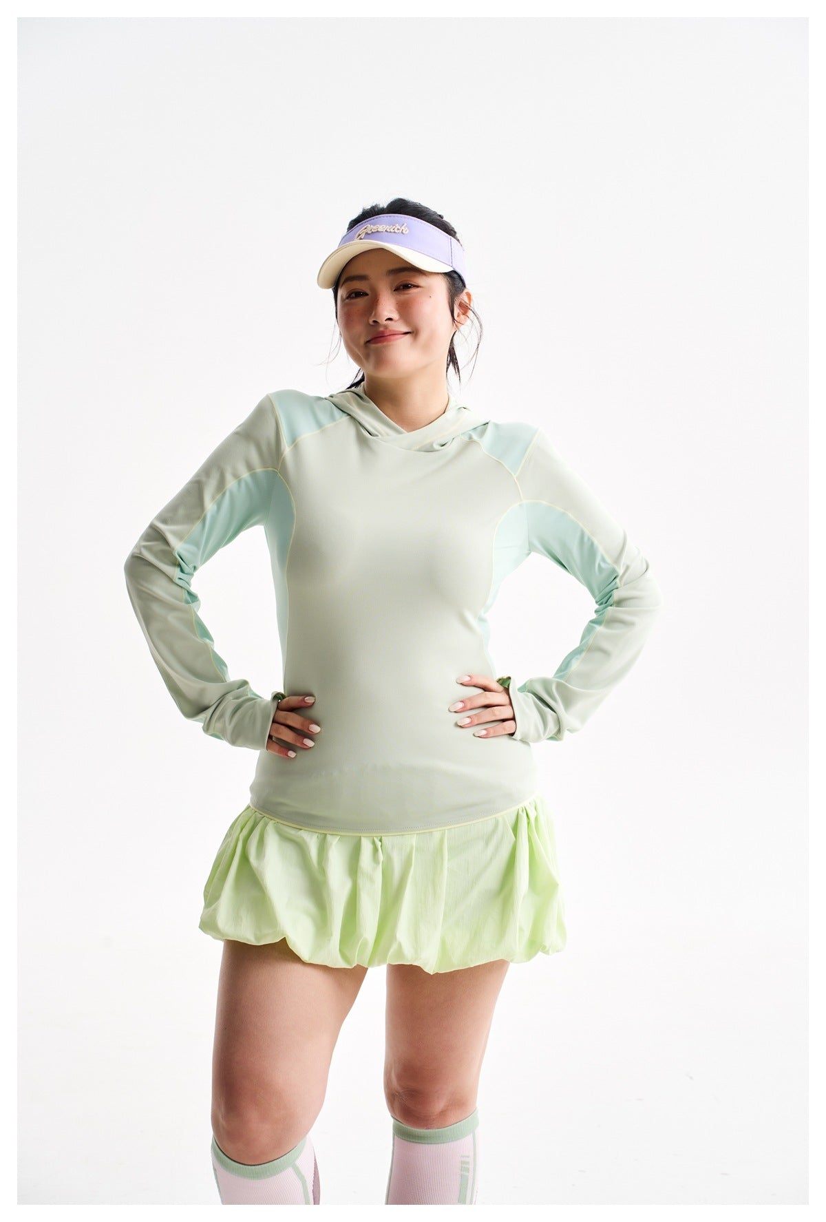Closer front view of a model wearing a pale mint hooded top with aqua panels and a lime bubble-hem skirt.