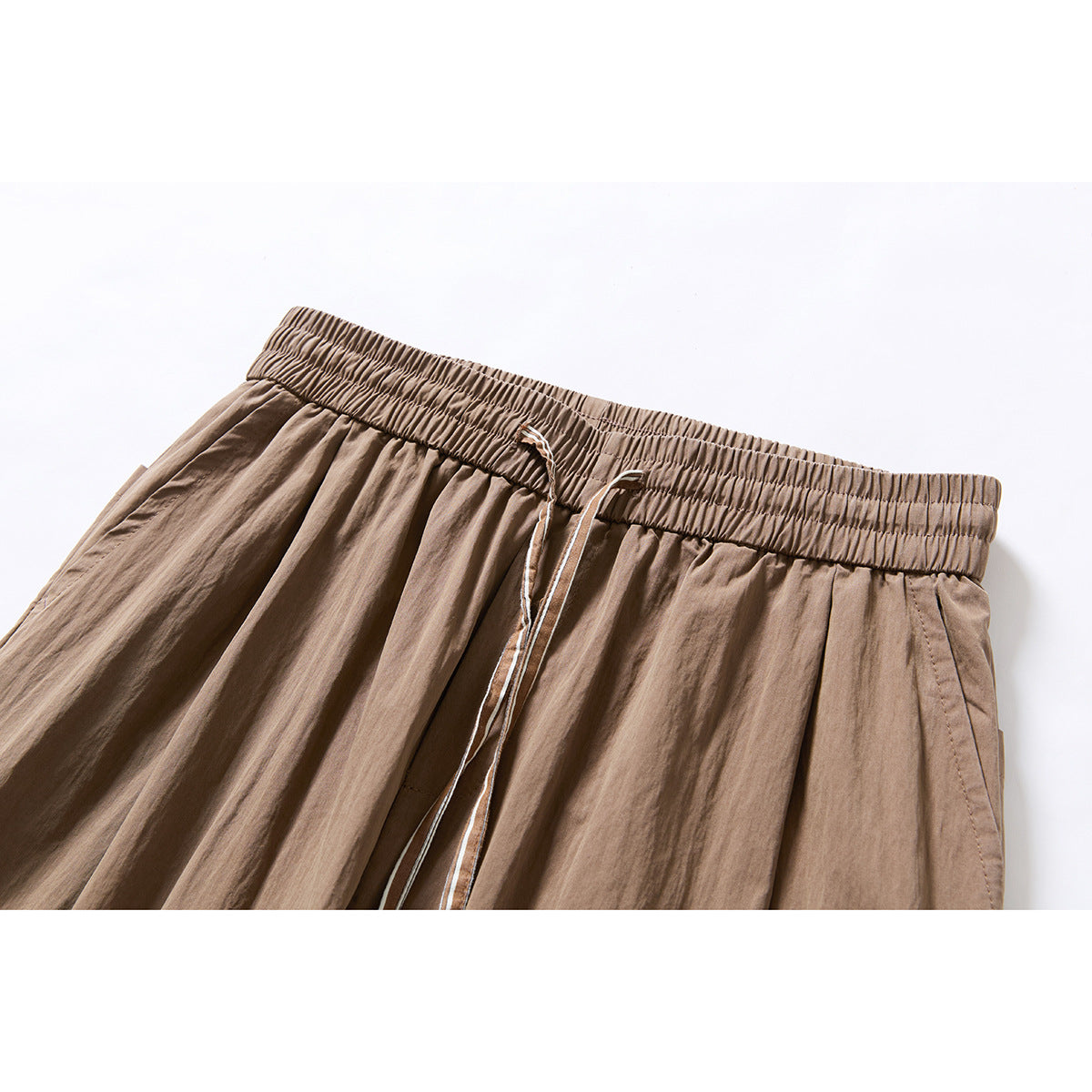Close-up of taupe wide-leg trousers showing an elastic waistband, drawstring, and front pleats.