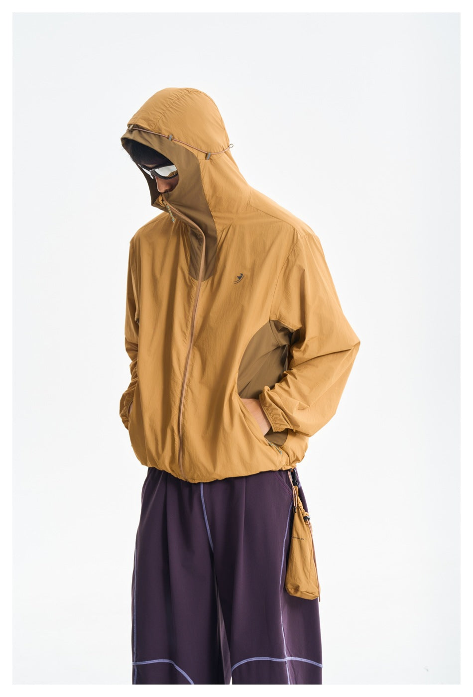 Model in a mustard hooded jacket and plum pants, shown at an angle with hands in the jacket pockets.