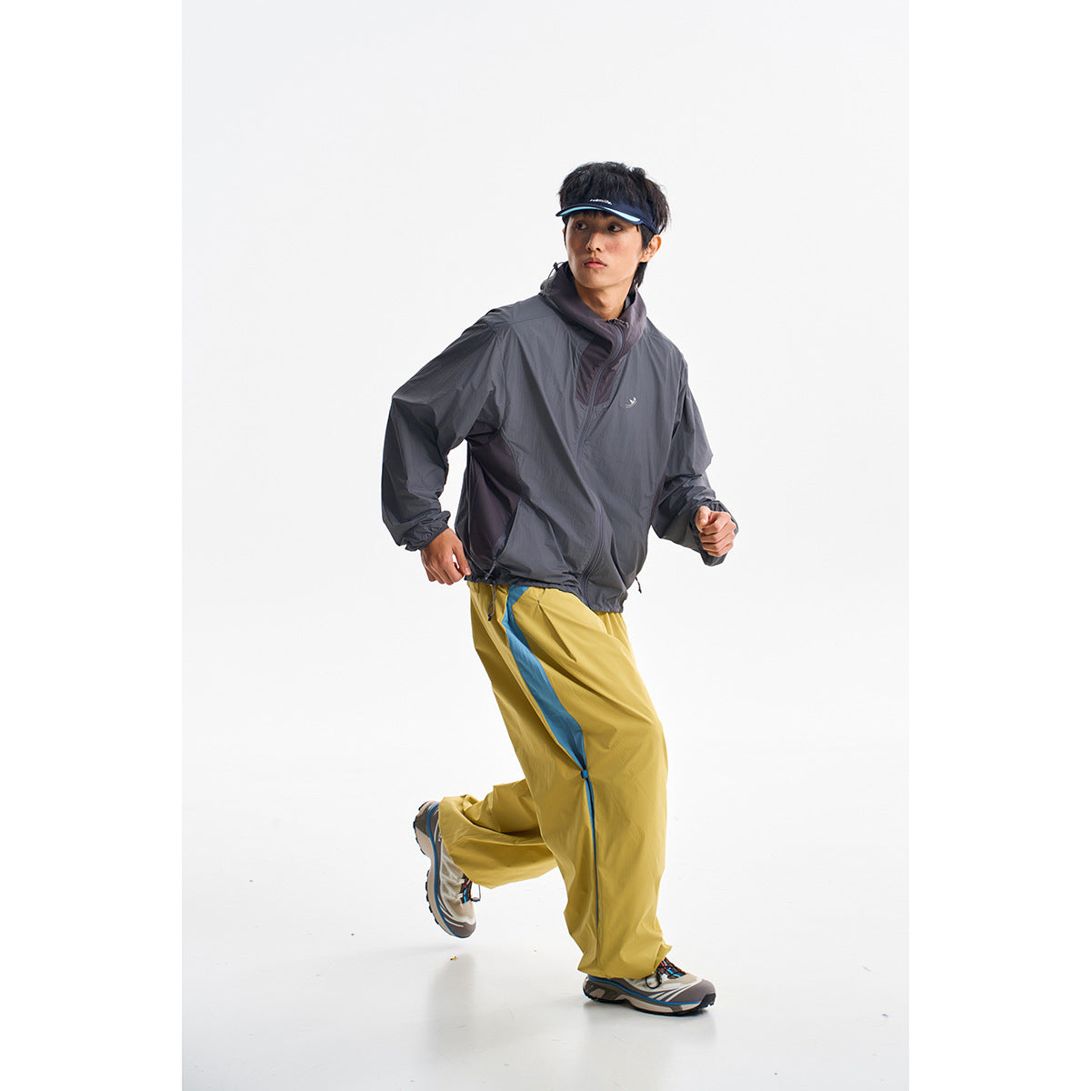 Model running in a dark gray pullover jacket and mustard yellow trousers with blue side stripes.