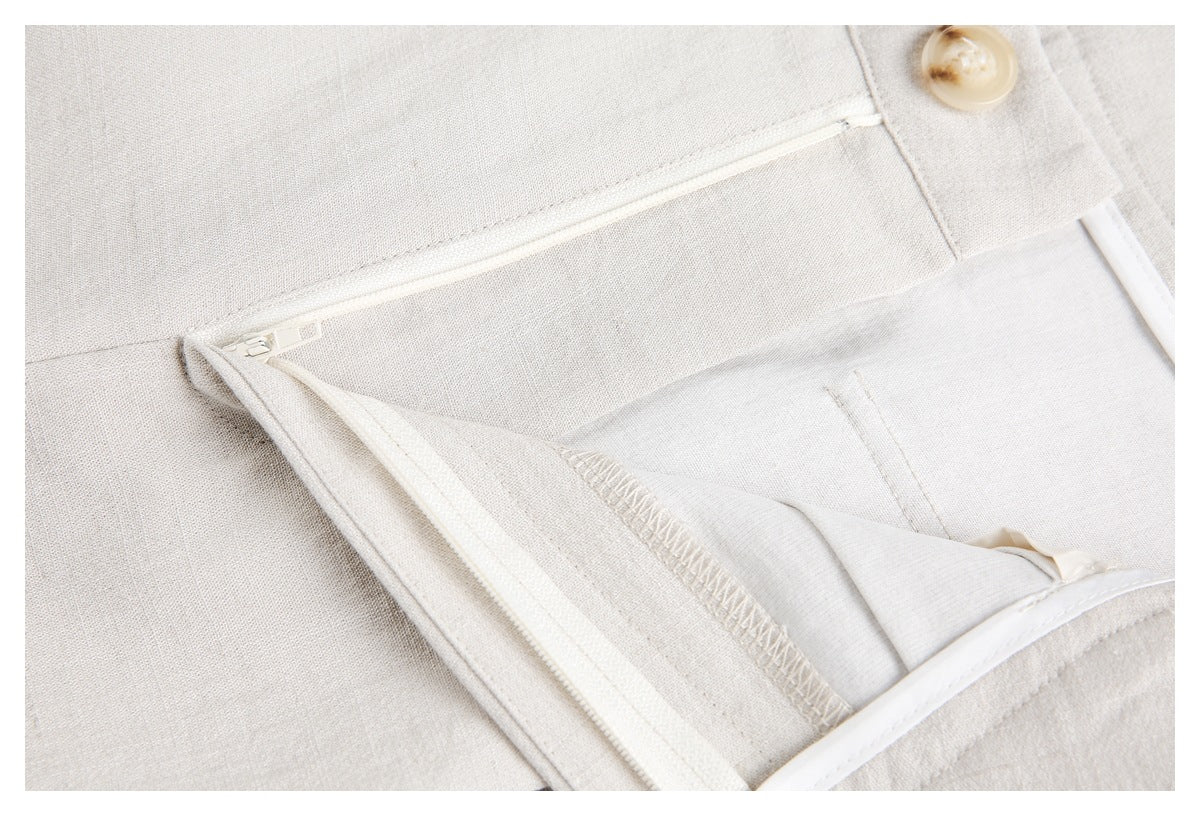 Inside close-up of ivory trousers showing the zipper fly, button, waistband stitching, and seam finishing.