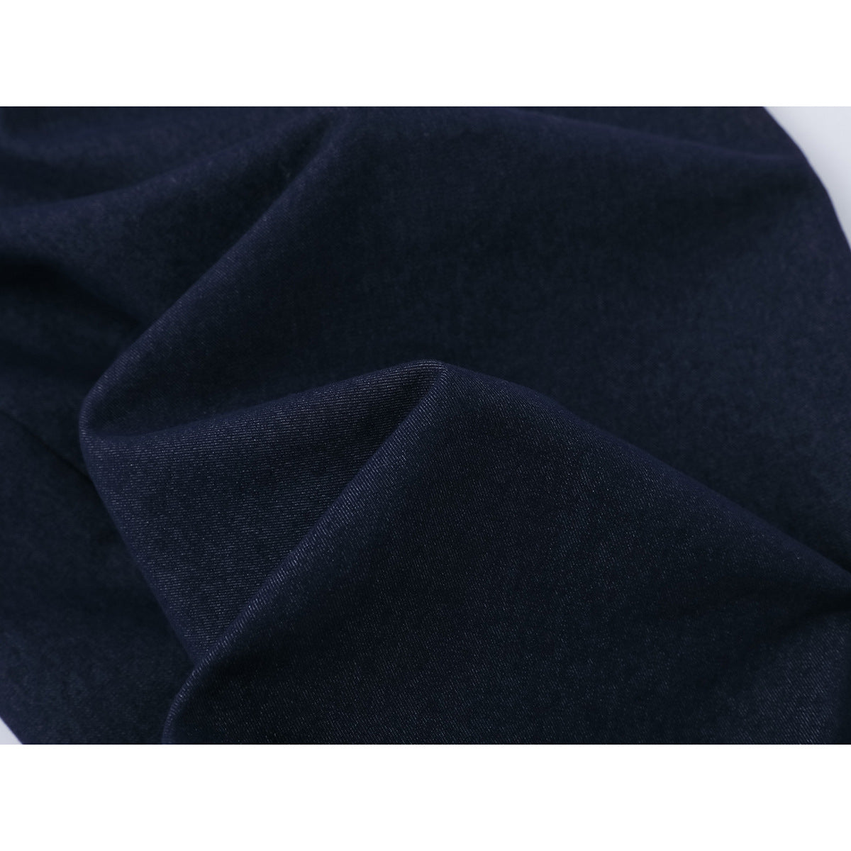 Close-up of dark navy trouser fabric arranged in folds, revealing its fine surface texture.