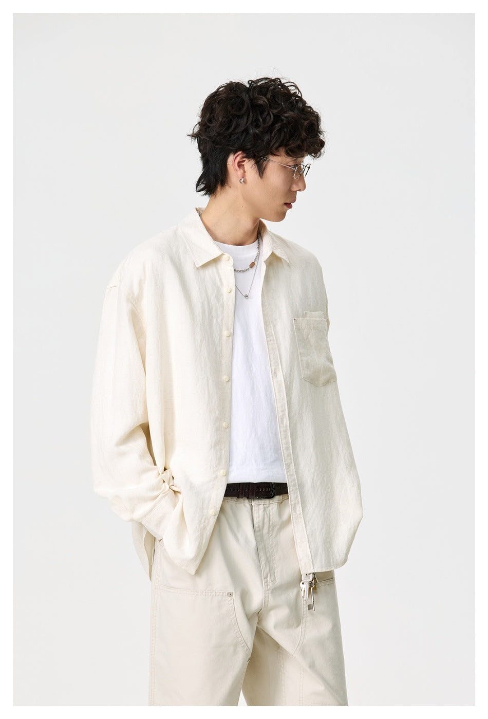 Three-quarter view of a model wearing an open ivory shirt with a chest pocket and cream trousers.