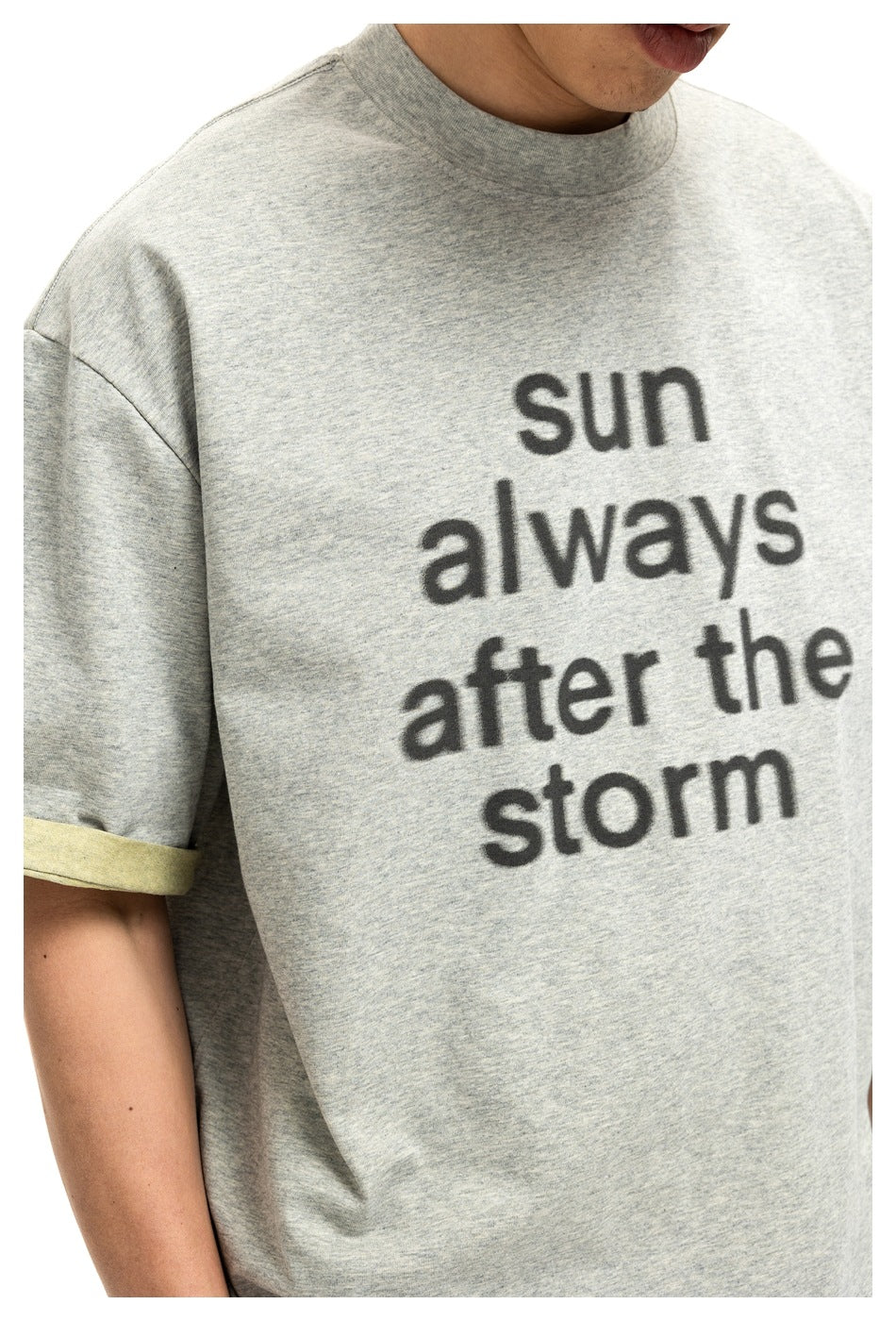 Close-up of a gray T-shirt with black “sun always after the storm” lettering and a pale yellow sleeve cuff.