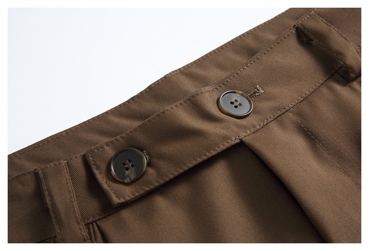 Close-up of brown trousers showing the waistband, belt loop, and two dark buttons.