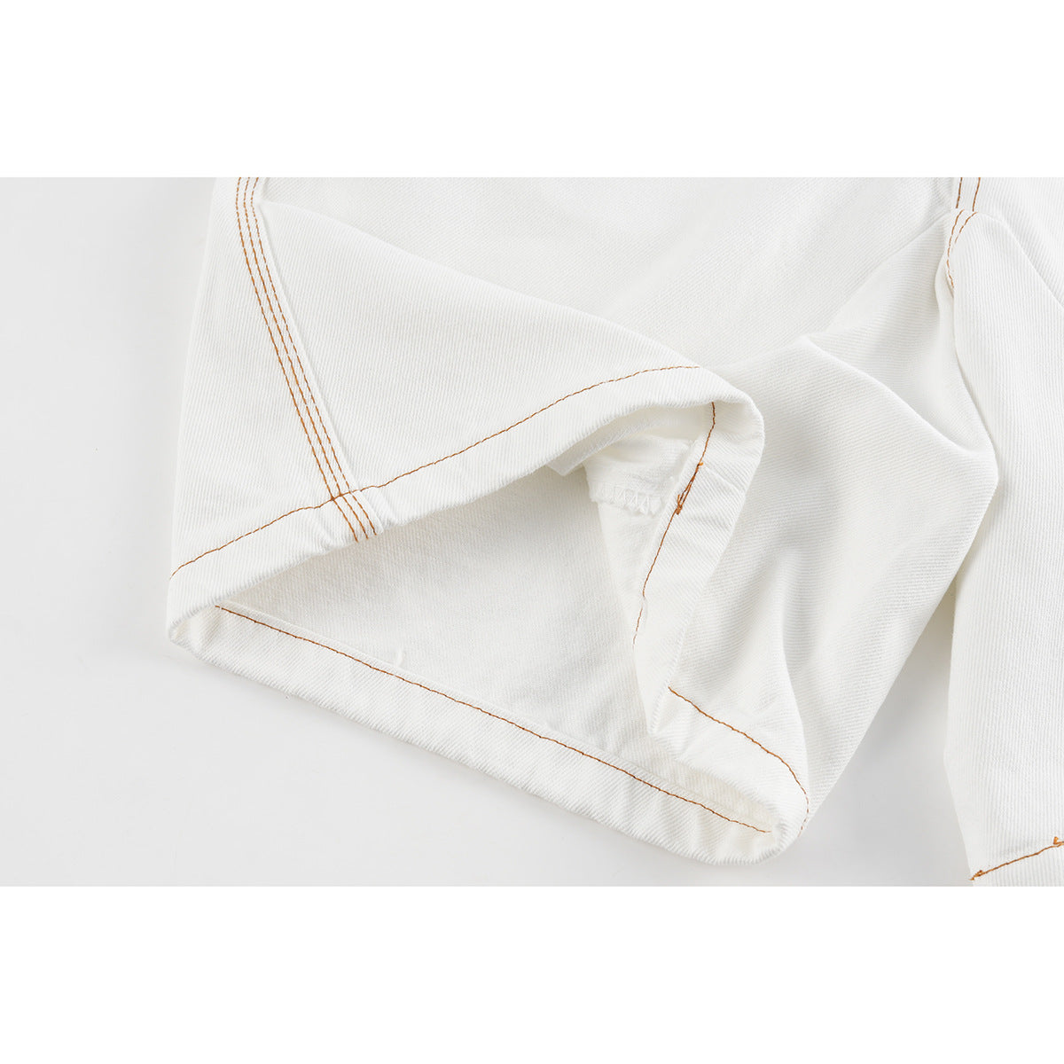 Close-up of the turned-up hem and orange-brown seams on white denim shorts.