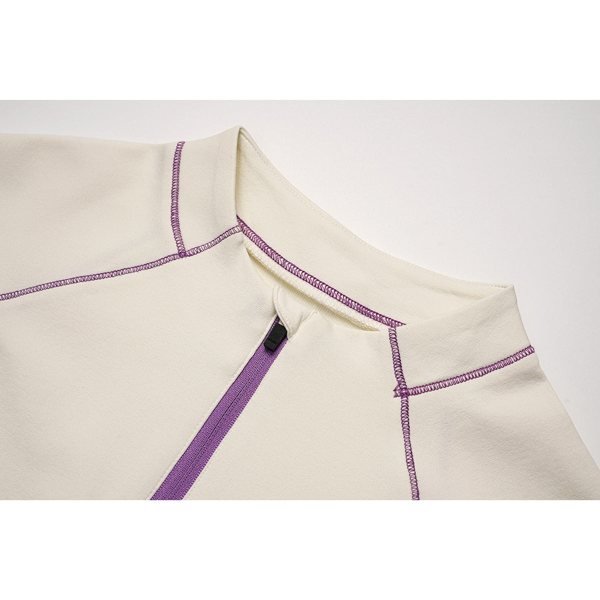Close-up of an ivory top's stand collar, purple zipper, and purple overlock stitching.