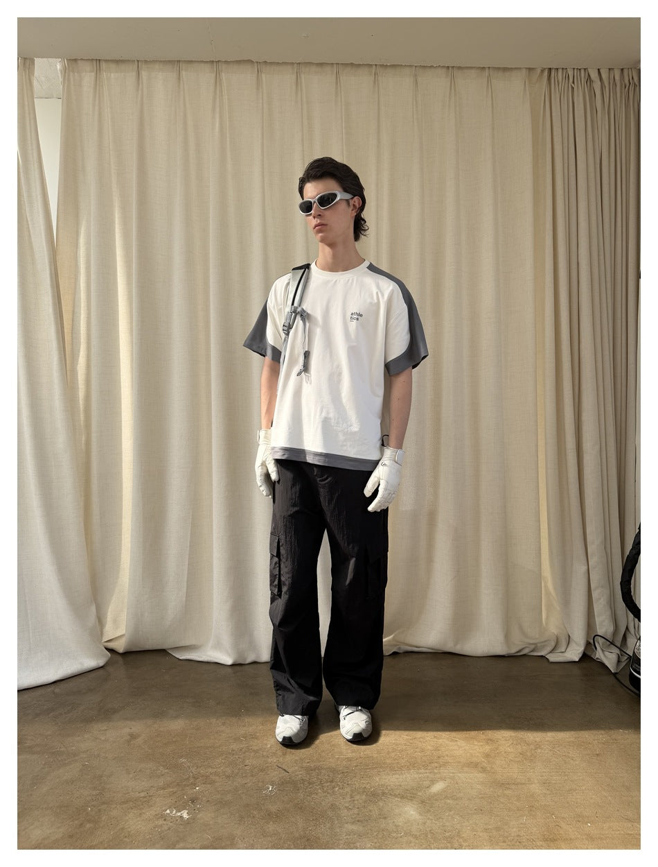Full-length view of a model wearing a white T-shirt with dark gray panels and black cargo pants.