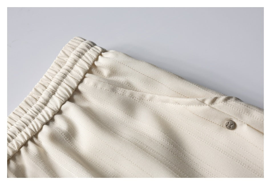 Close-up of cream striped trousers showing the elastic waistband and a small button.