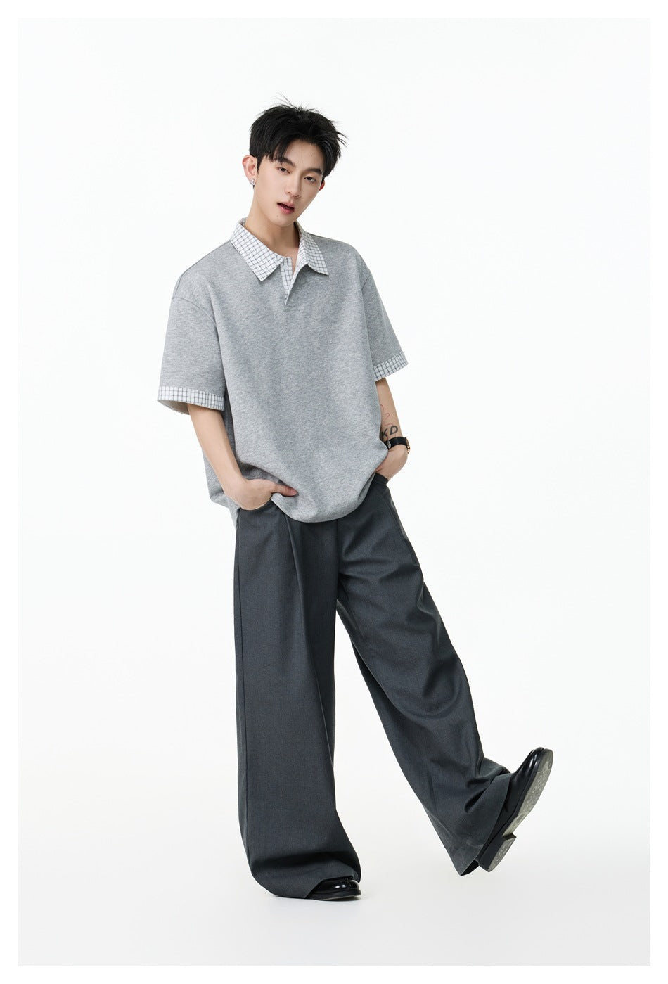 Model wearing an oversized heather-gray polo with a checked collar and cuffs, paired with wide dark trousers.