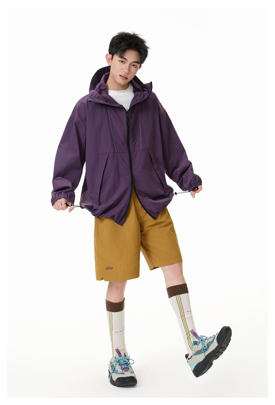 Model wearing an open-collar plum hooded jacket and mustard shorts, with the hem drawcords visible.