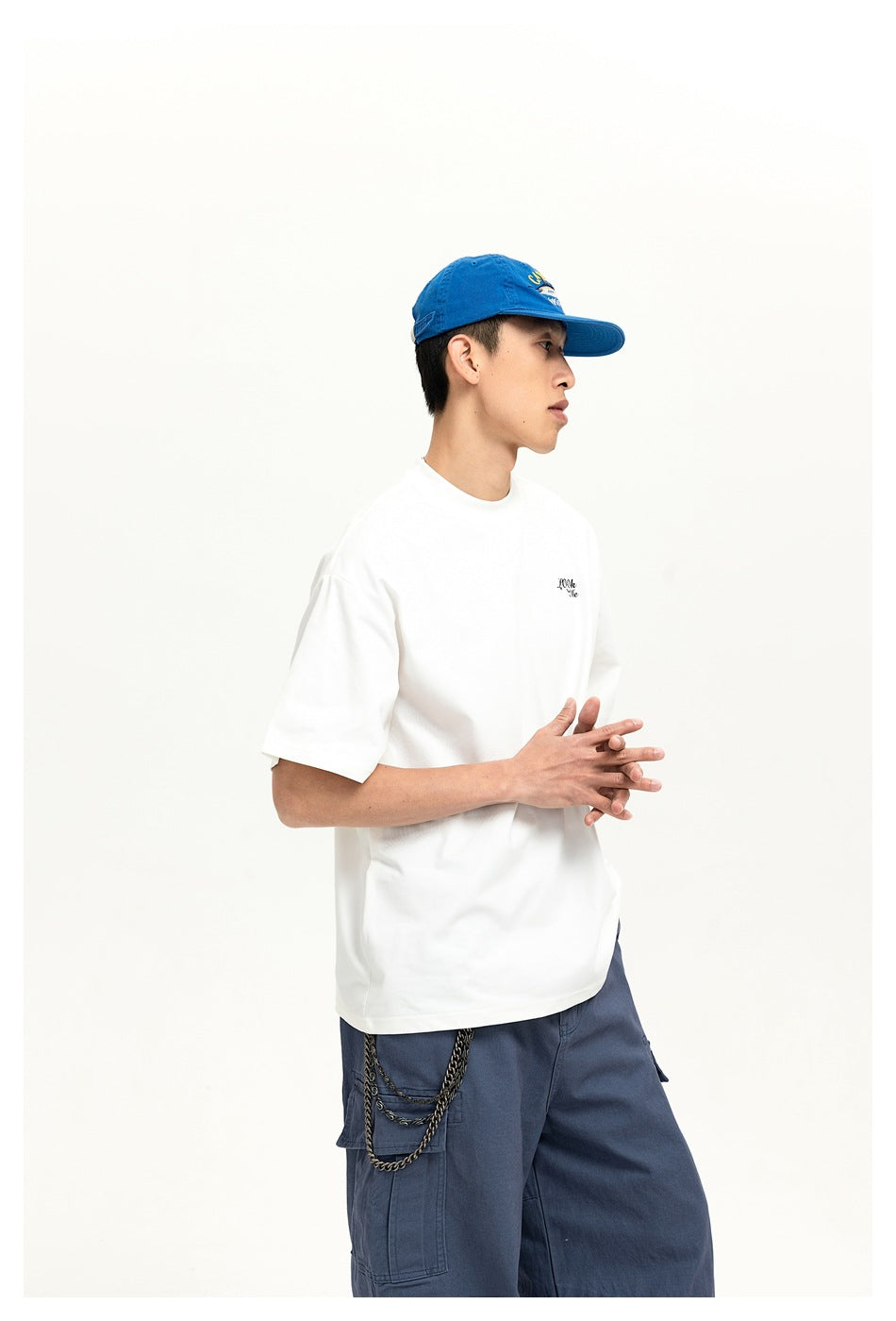Side view of a model in a white boxy T-shirt with drop shoulders, blue cap and blue cargo pants
