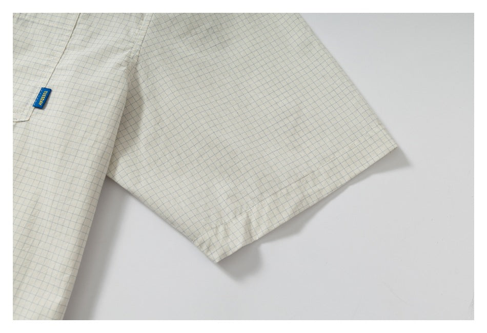 Close-up of the short sleeve and hem stitching on a cream shirt with a fine blue grid.