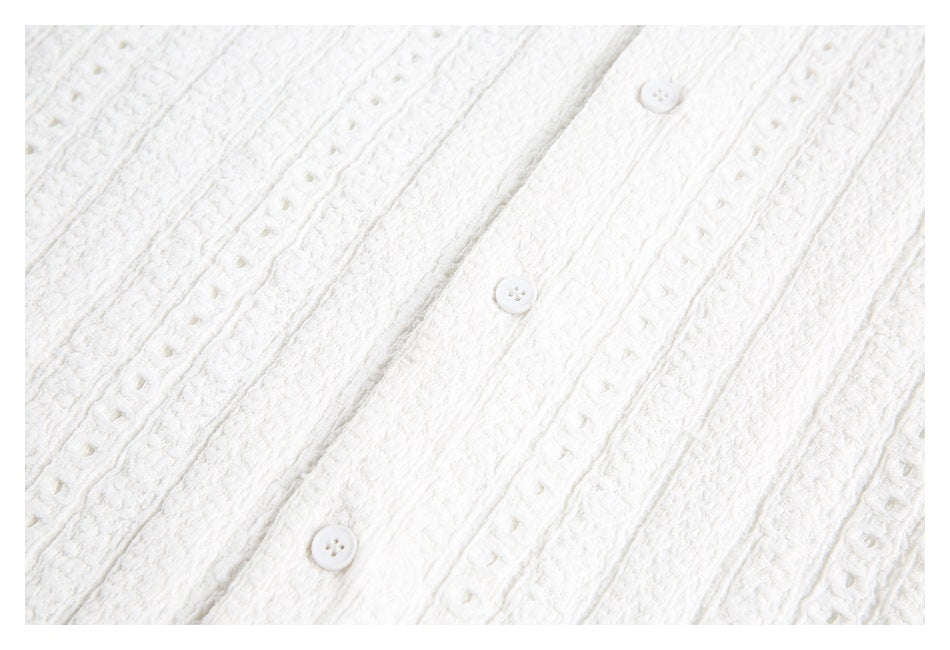 Close-up of white textured garment with vertical eyelet bands and small white buttons.