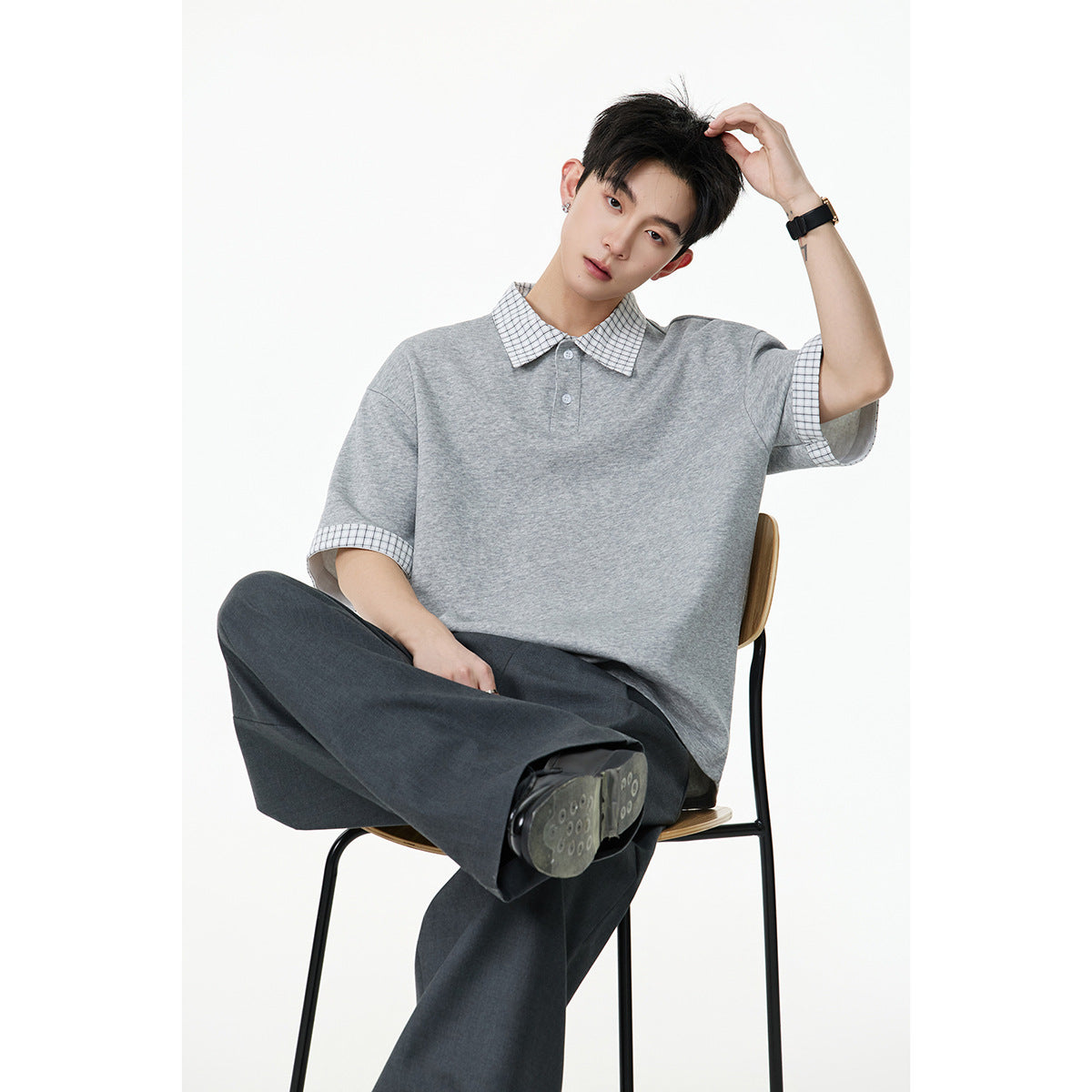 Seated model wearing an oversized heather-gray polo with a small checked collar and sleeve cuffs.