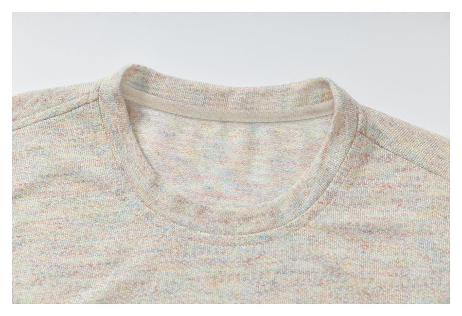 Close-up of the crew neckline and shoulder seams on a pale pastel-flecked T-shirt.
