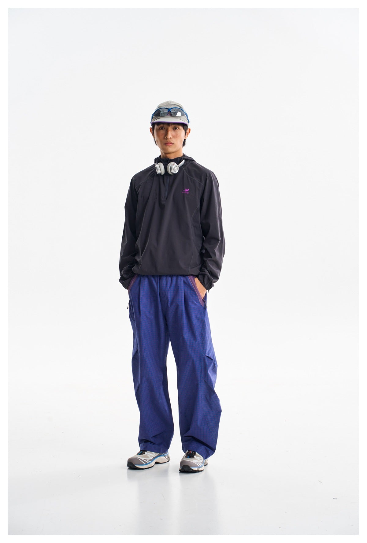 Front view of a model wearing loose blue-purple checked trousers and a dark pullover jacket.