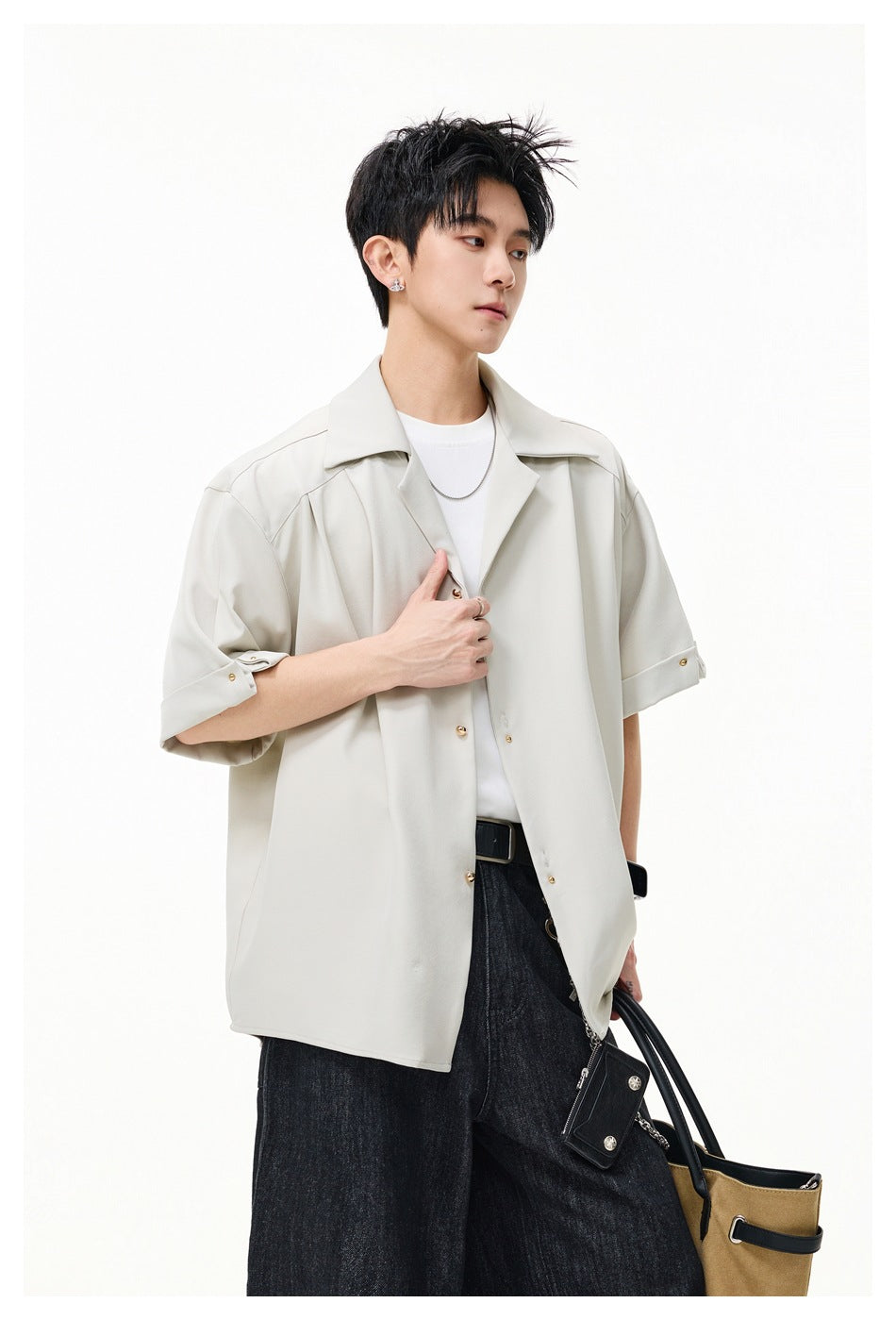 Model wearing an open light cream short-sleeve shirt with wide lapels and rolled cuffs over a white T-shirt.