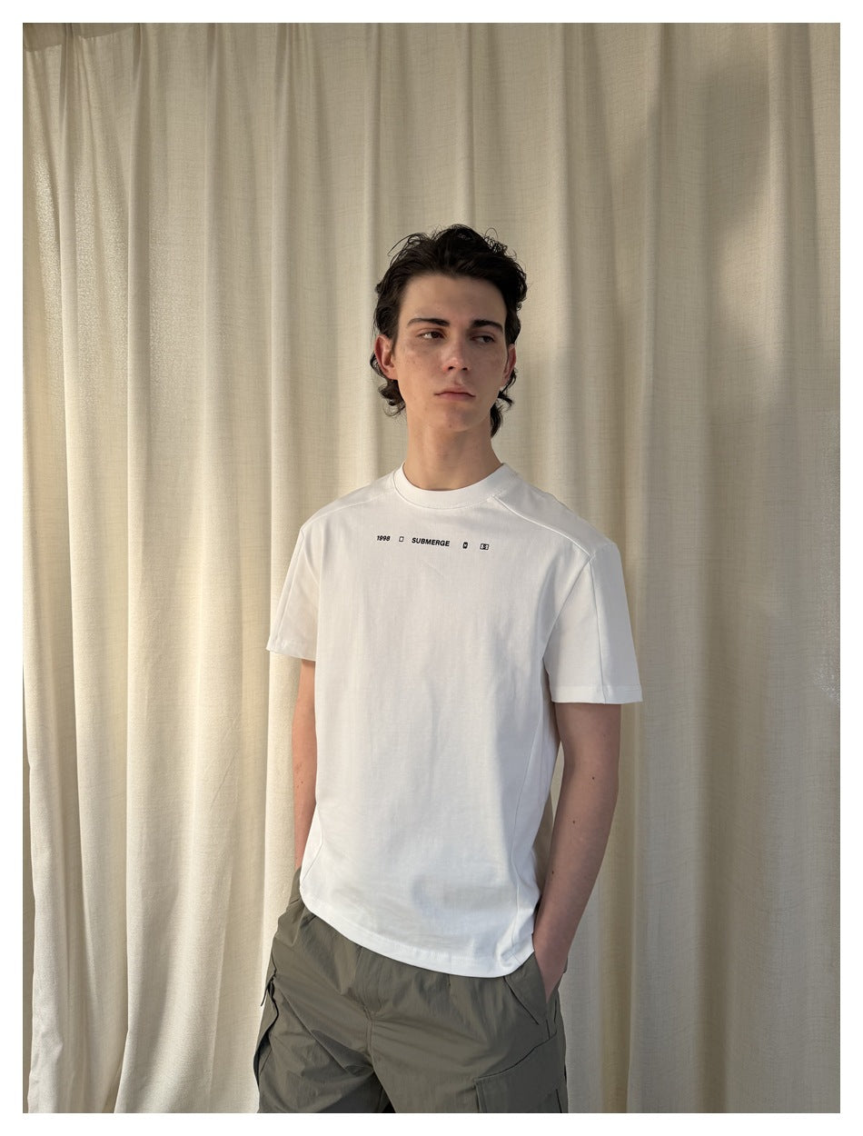 Model wearing a white short-sleeve crew-neck T-shirt with small black chest text and symbols.