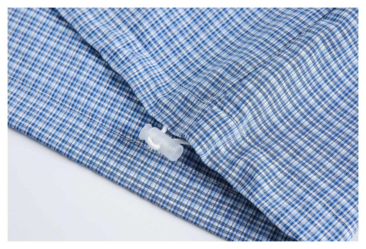 Blue-and-white checked garment close-up with a small translucent plastic fastener beside a seam.