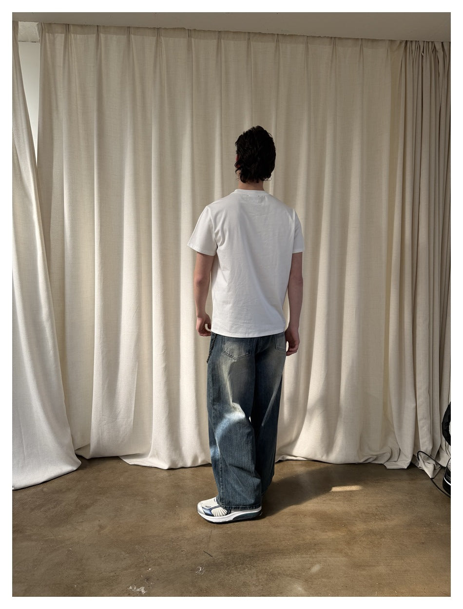 Back view of a person wearing a plain white short-sleeve T-shirt with faded wide-leg jeans in front of cream curtains