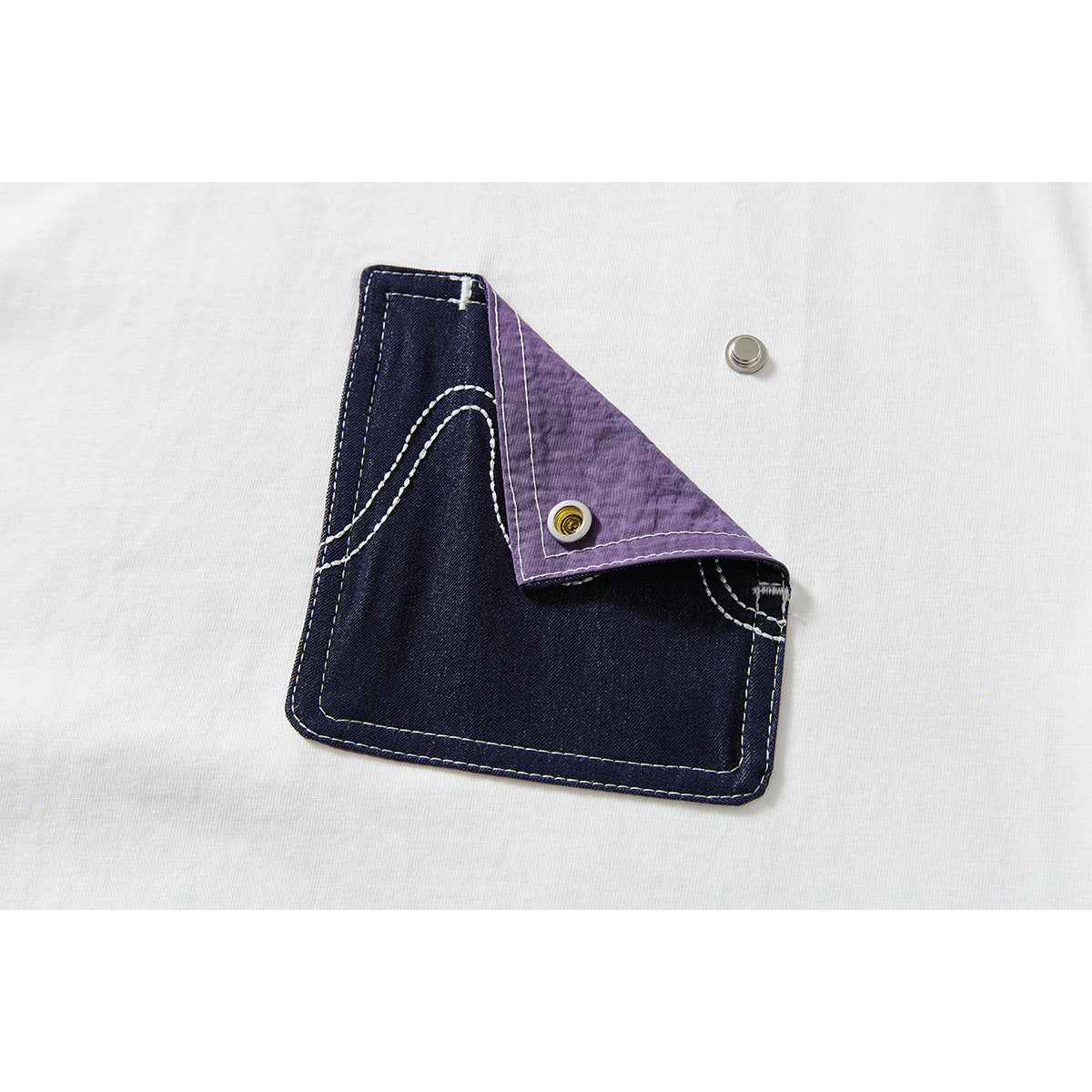 Close-up of a dark indigo pocket with white stitching and a folded purple flap on a white T-shirt.