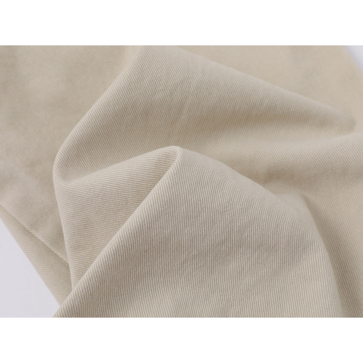 Close-up of beige trouser fabric arranged in folds, showing its fine diagonal weave.