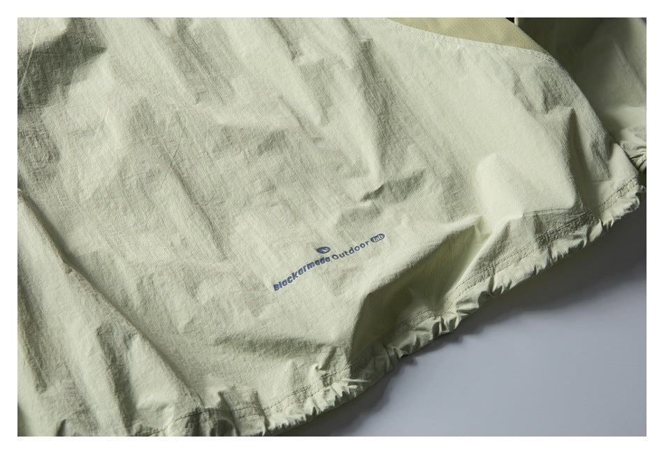Pale sage garment panel with a small blue Blackmamba Outdoor Lab print and gathered stitched hem.