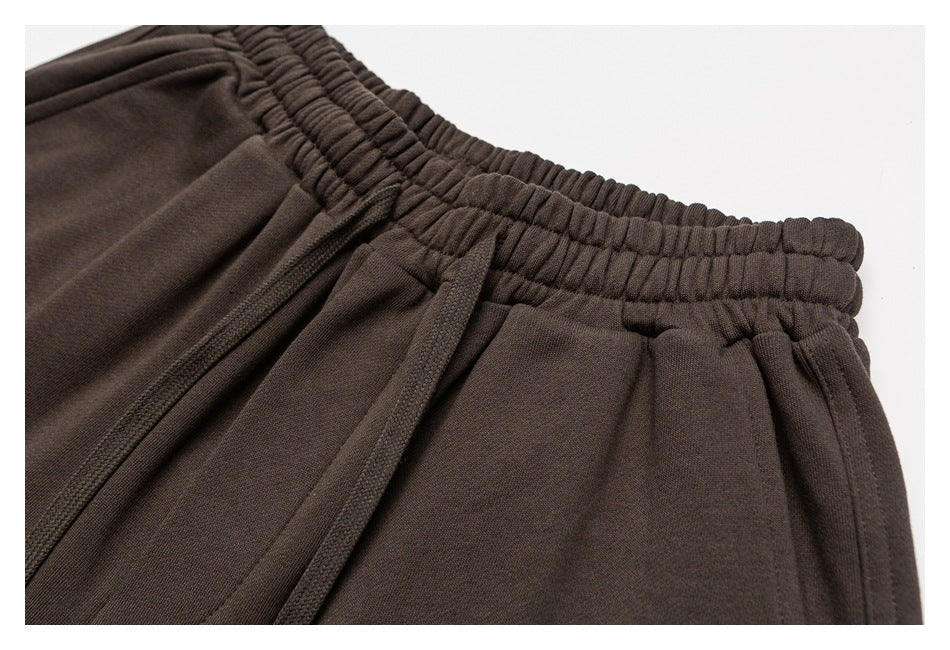 Close-up of dark brown sweatpants showing the gathered elastic waistband, drawstring and pocket opening.