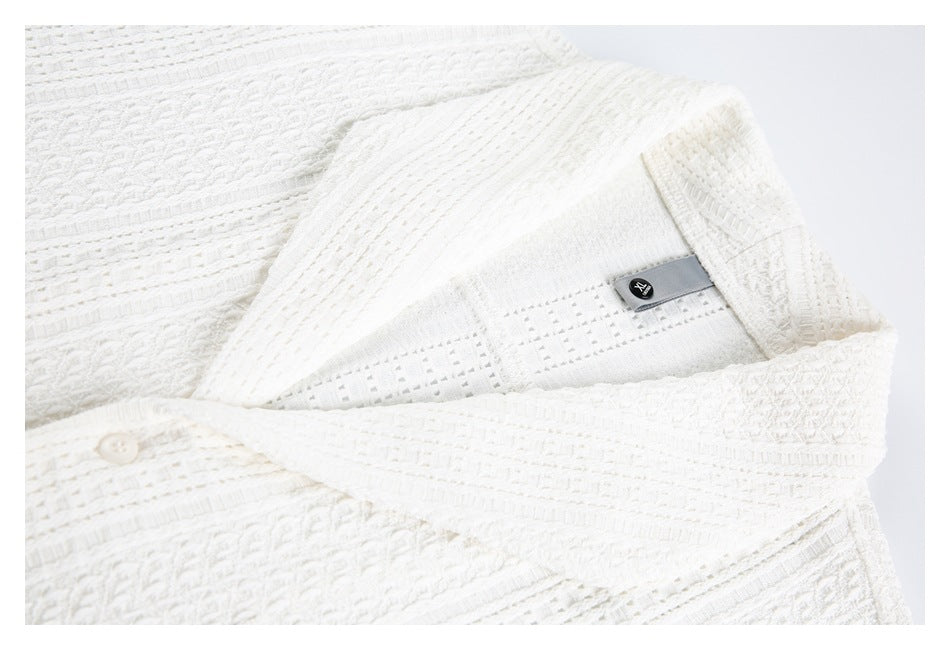 Close-up of a white tunic collar, inner label, openwork texture, and button.