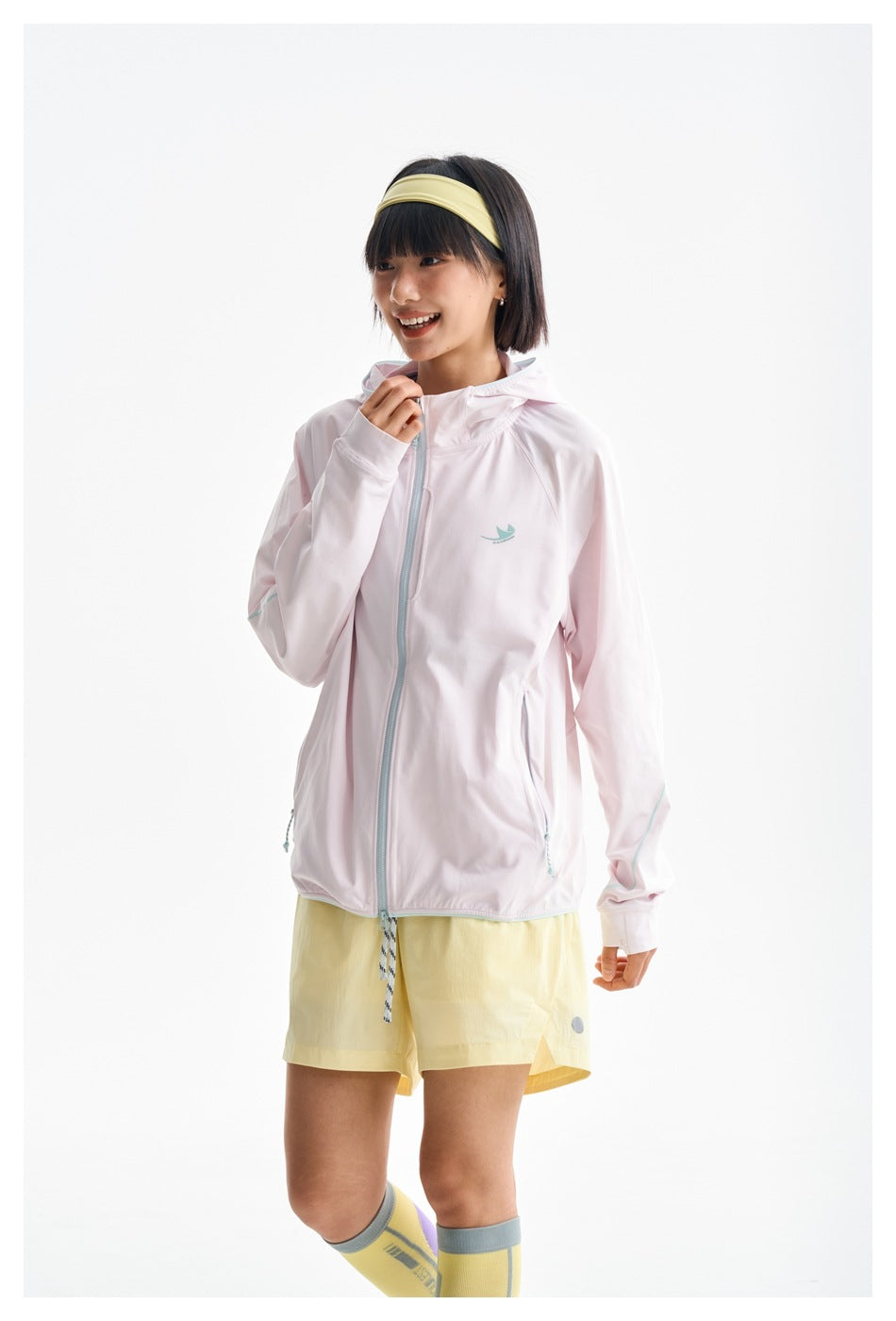 Model wearing a pale pink hooded zip jacket with aqua trim and yellow shorts, shown from the front.