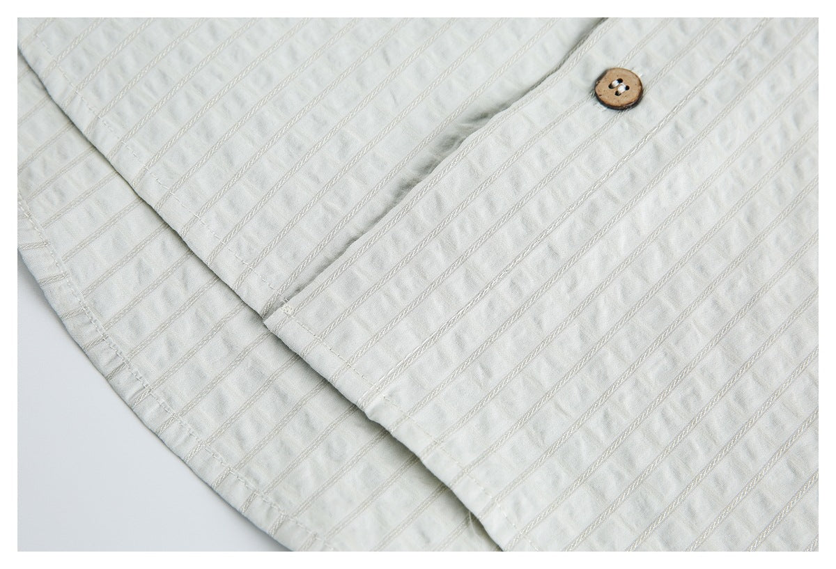 Ivory striped garment close-up showing a brown button, overlapping fabric, and stitched detailing.
