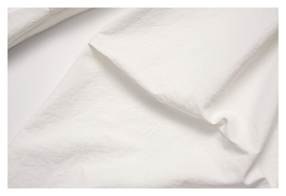 Close-up of off-white garment fabric draped in soft folds, showing a subtle fine texture.