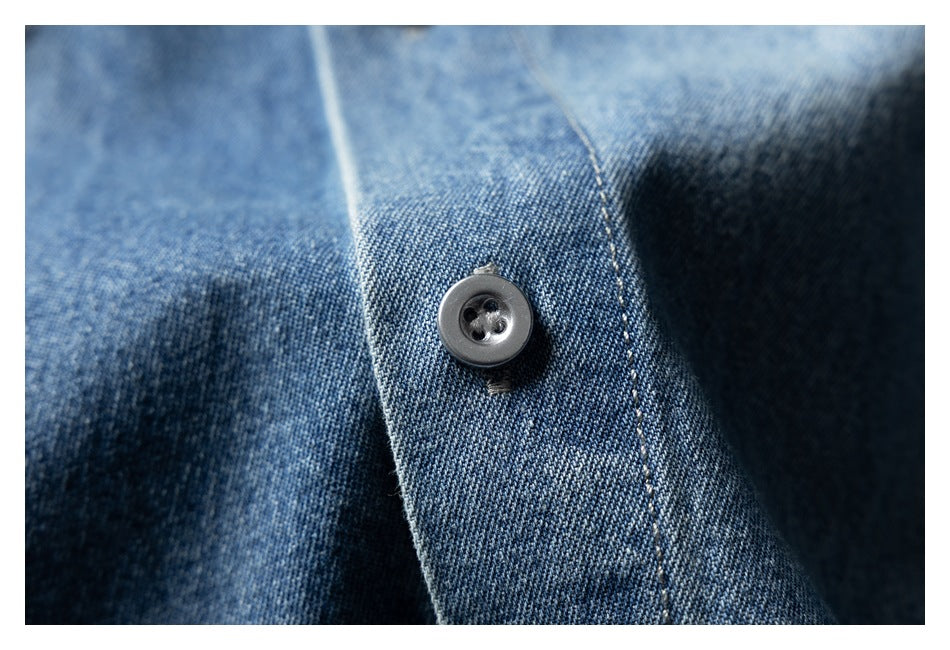Macro view of a dark four-hole button sewn onto the blue denim shirt placket.