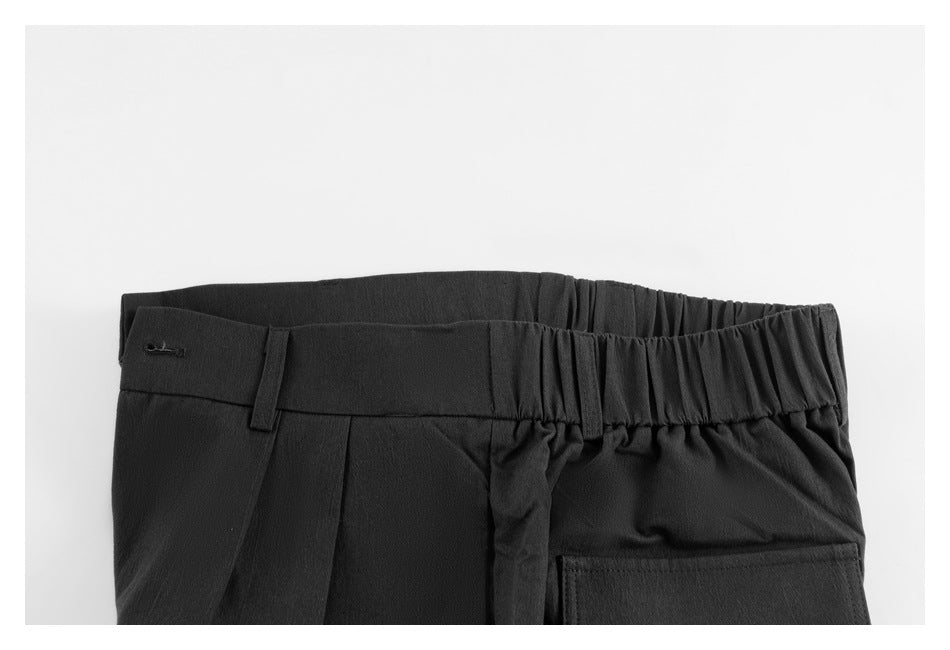 Close-up of the back waistband of black trousers, with elastic gathering, belt loops, and a rear pocket.