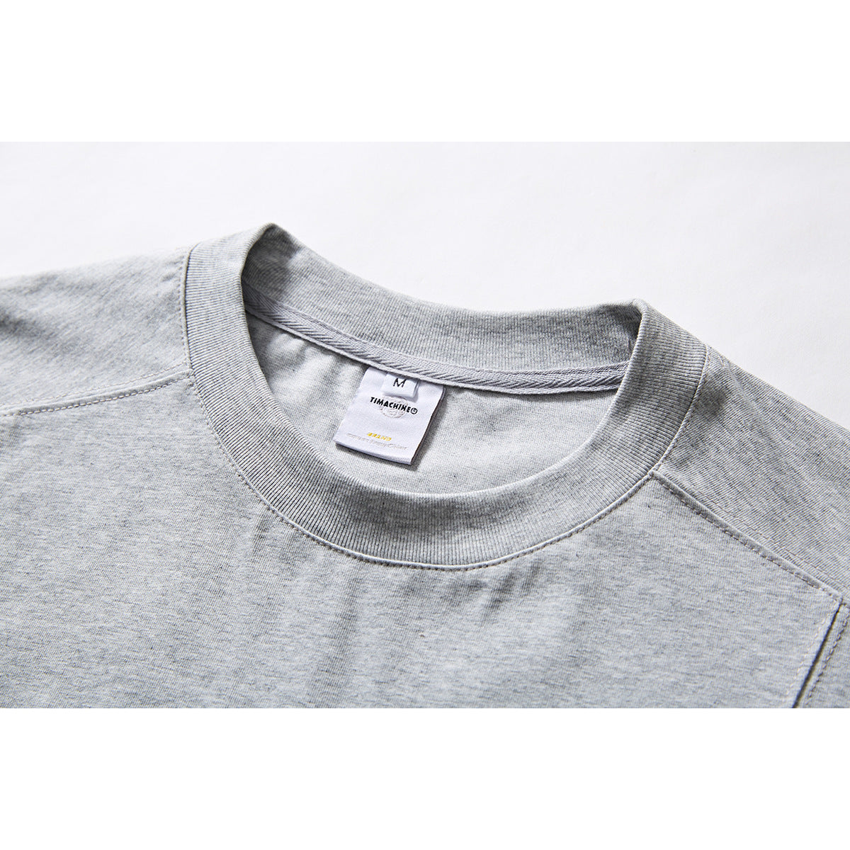 Close-up of a light gray T-shirt’s ribbed crew neck, shoulder seams, and inner label.