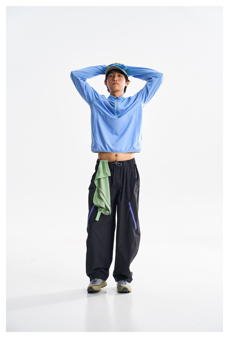 Model wearing a light blue quarter-zip pullover and black pants, front view with arms raised and hem lifted.