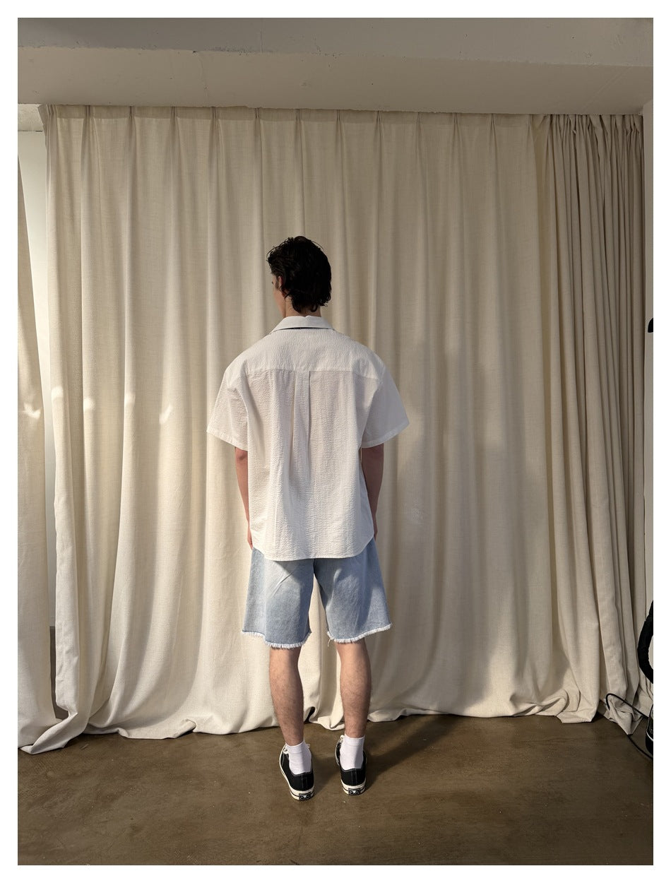 Back view of a model wearing a white short-sleeve shirt and light denim shorts.