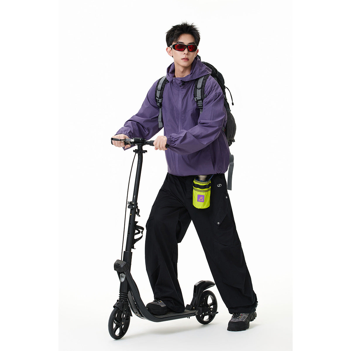 Model wearing a purple hooded jacket and black cargo pants while standing on a scooter with a backpack.
