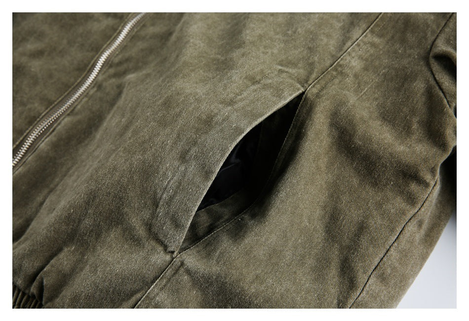 Close-up of an olive-gray garment showing a diagonal zipper and an open side pocket.