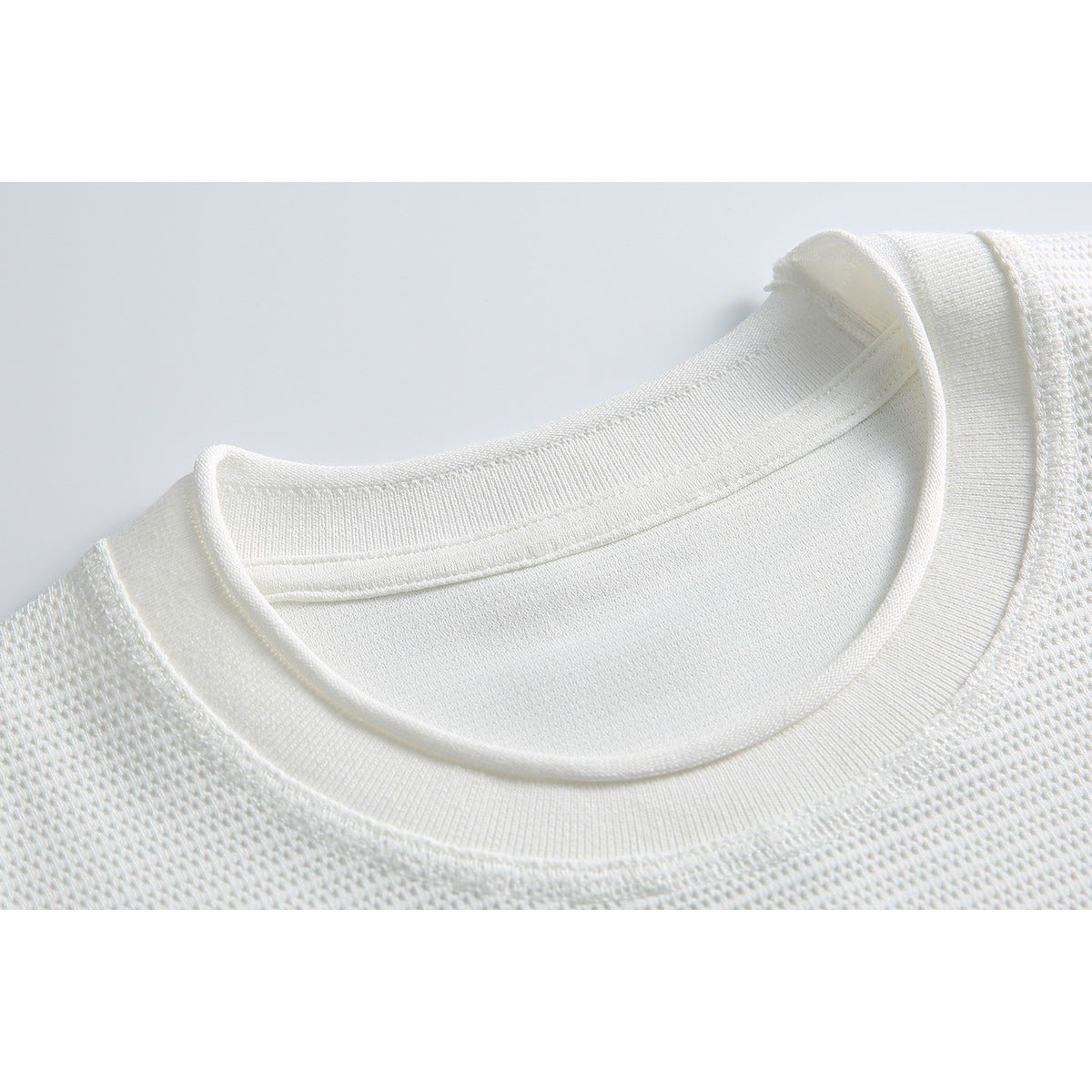 Close-up of a white T-shirt’s ribbed crew neckline and textured knit fabric.